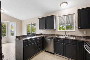 Kitchen featuring a peninsula, range, light tile patterned flooring, dishwasher, and dark cabinetry