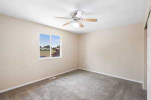 Carpeted empty room featuring a ceiling fan and baseboards