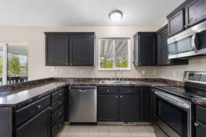 Kitchen featuring stainless steel appliances, a peninsula, light tile patterned floors, dark cabinets, and dark stone countertops