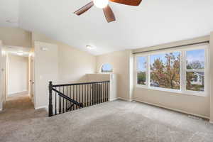 Spare room with carpet floors, a ceiling fan, and vaulted ceiling