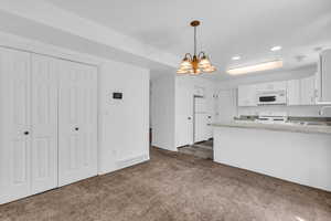Kitchen featuring hanging lights, light countertops, white cabinetry, a peninsula, and white appliances