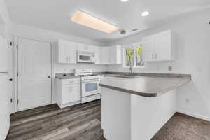 Kitchen with a peninsula, white cabinetry, white appliances, a breakfast bar, and recessed lighting