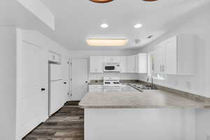 Kitchen with a peninsula, white cabinets, white appliances, light countertops, and LVP flooring