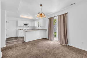 Kitchen featuring hanging lights, a peninsula, white cabinetry, dark colored carpet, and light countertops