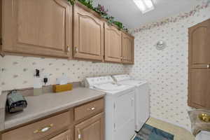 Laundry room featuring wallpapered walls, washer and clothes dryer, and cabinet space