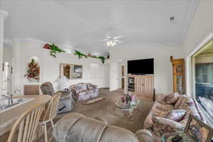 Carpeted living room featuring lofted ceiling, arched walkways, a ceiling fan, and crown molding