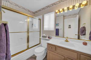 Full bath featuring vanity, wallpapered walls, and bath / shower combo with glass door