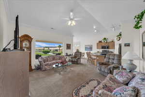 Living area featuring ceiling fan, light carpet, crown molding, and vaulted ceiling