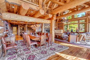 Dining space with log walls, light wood finished floors, suspended lighting, and a high wood beamed ceiling
