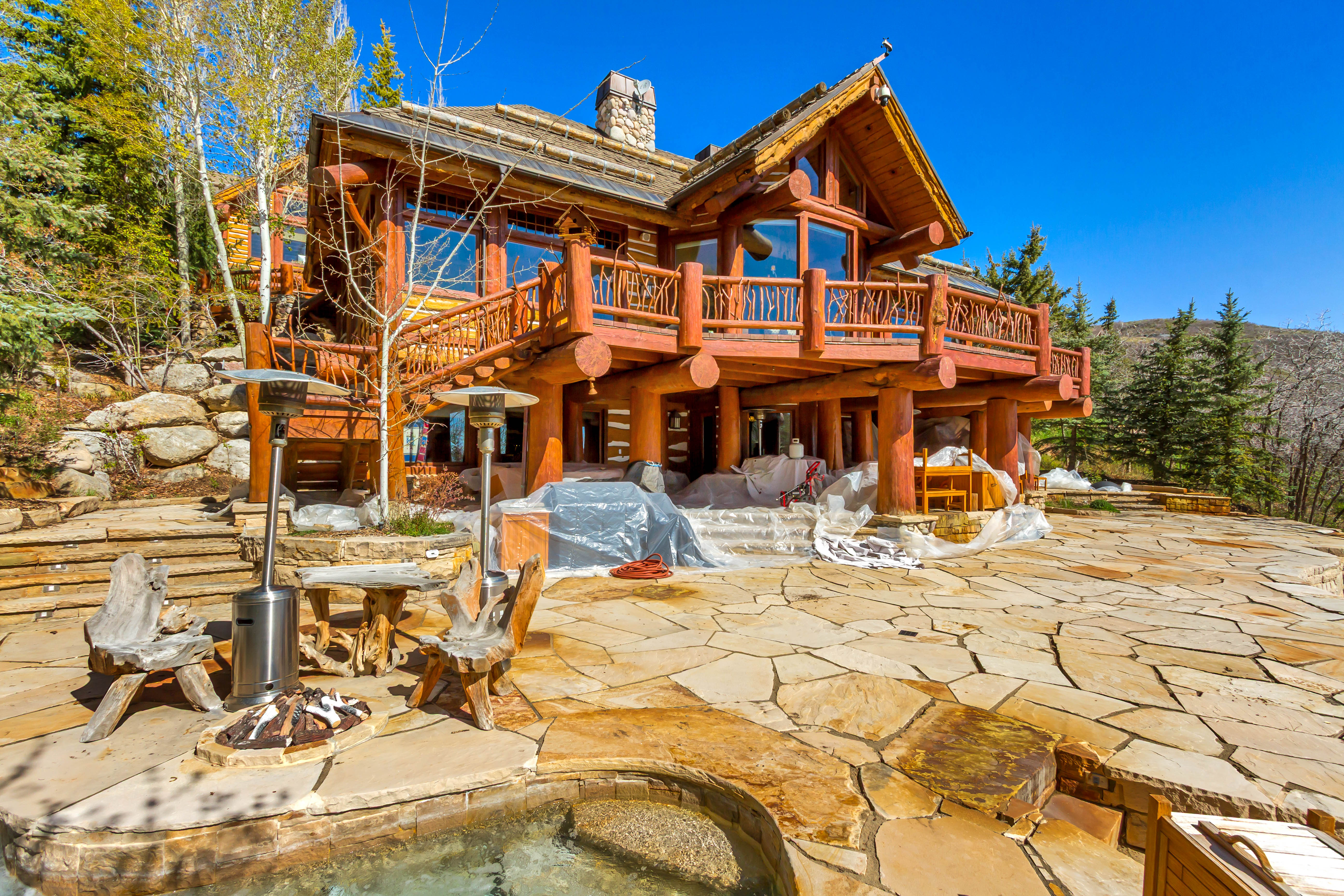 Back of house with a chimney, a patio, log exterior, a wooden deck, and a hot tub