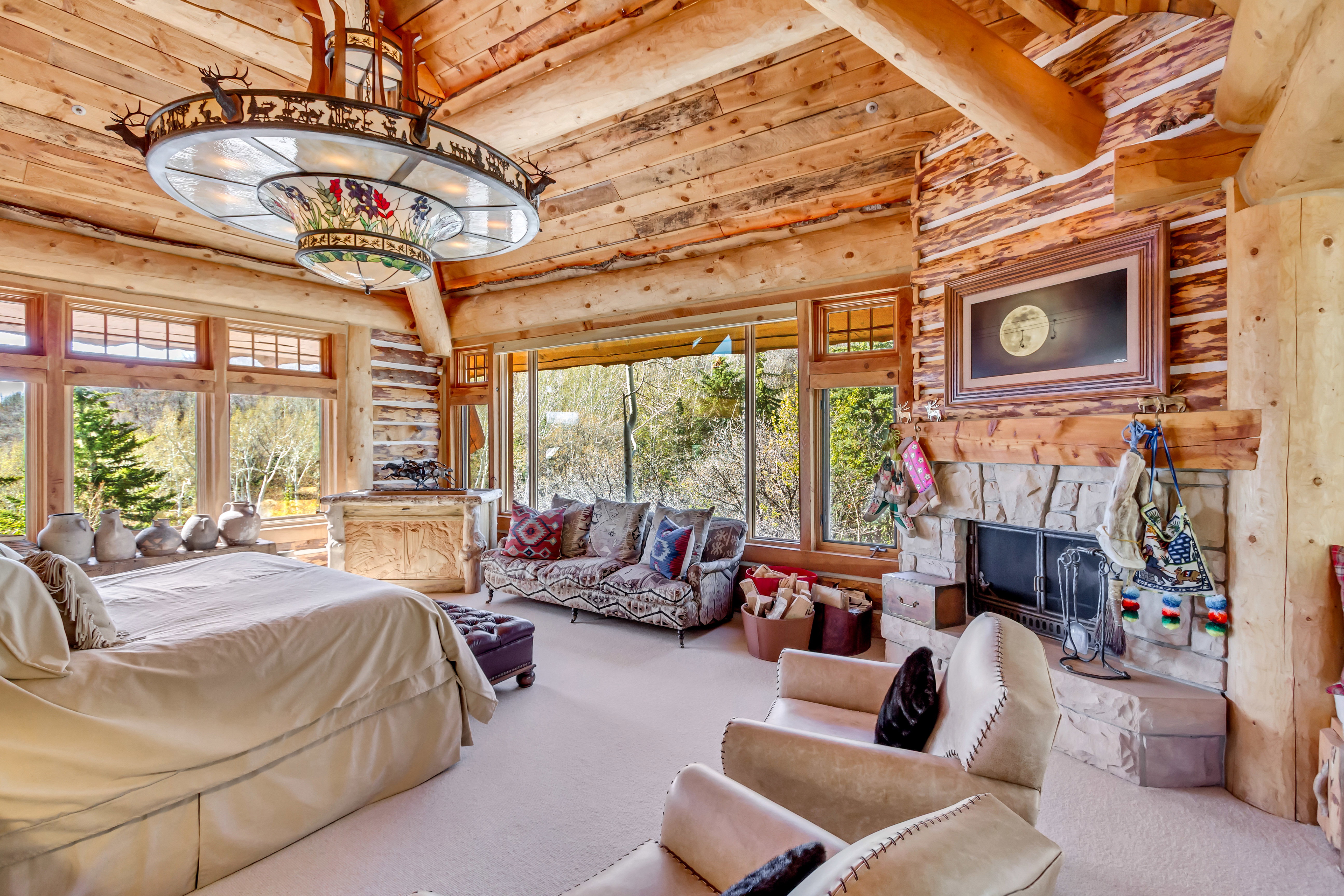 Carpeted bedroom with log walls, a stone fireplace, and a high wood beamed ceiling