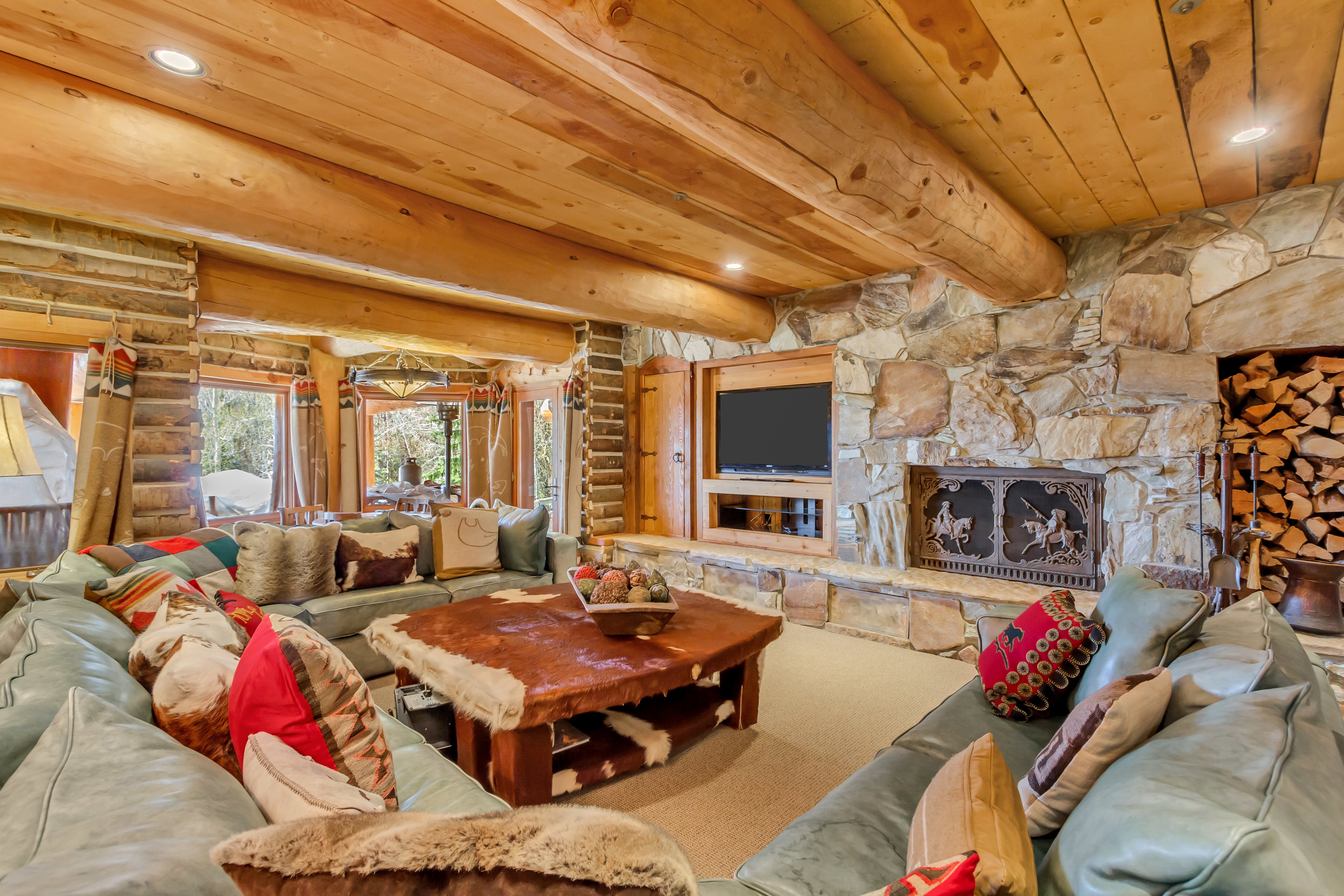 Living area featuring log walls, recessed lighting, a wood ceiling with exposed beams, carpet floors, and a stone fireplace