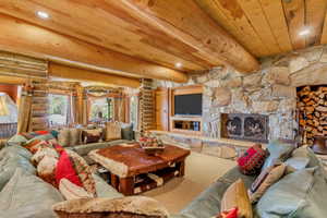 Living area featuring log walls, recessed lighting, a wood ceiling with exposed beams, carpet floors, and a stone fireplace