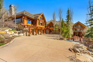 Cabin featuring stone siding, a chimney, concrete driveway, and log siding