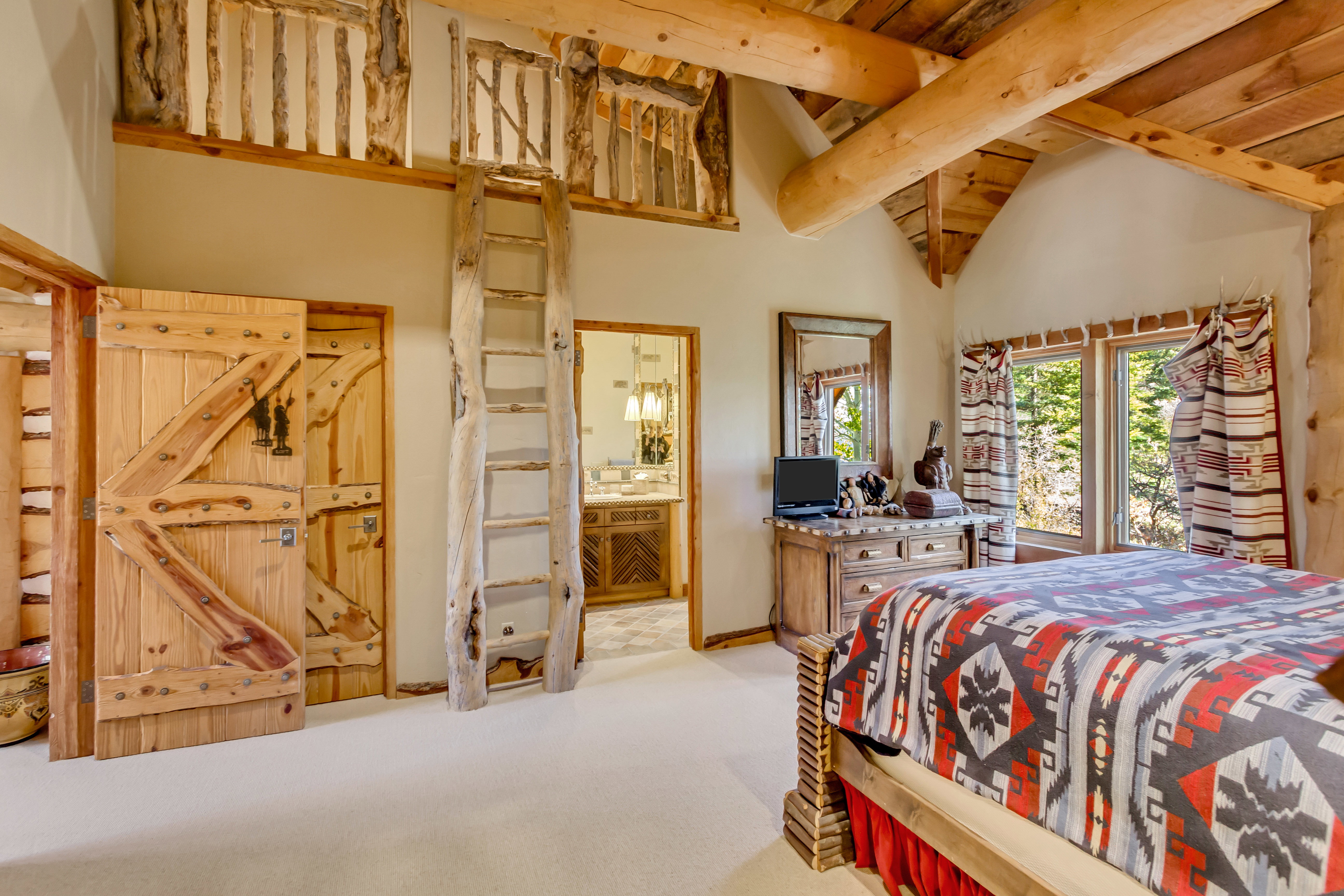 Bedroom with ensuite bathroom, a high wooden beamed ceiling, and light colored carpet