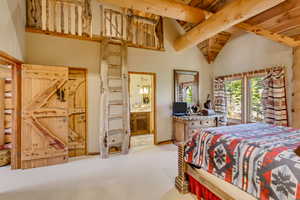 Bedroom with ensuite bathroom, a high wooden beamed ceiling, and light colored carpet