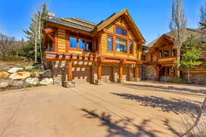 Log-style house with stone siding, driveway, a garage, and a chimney