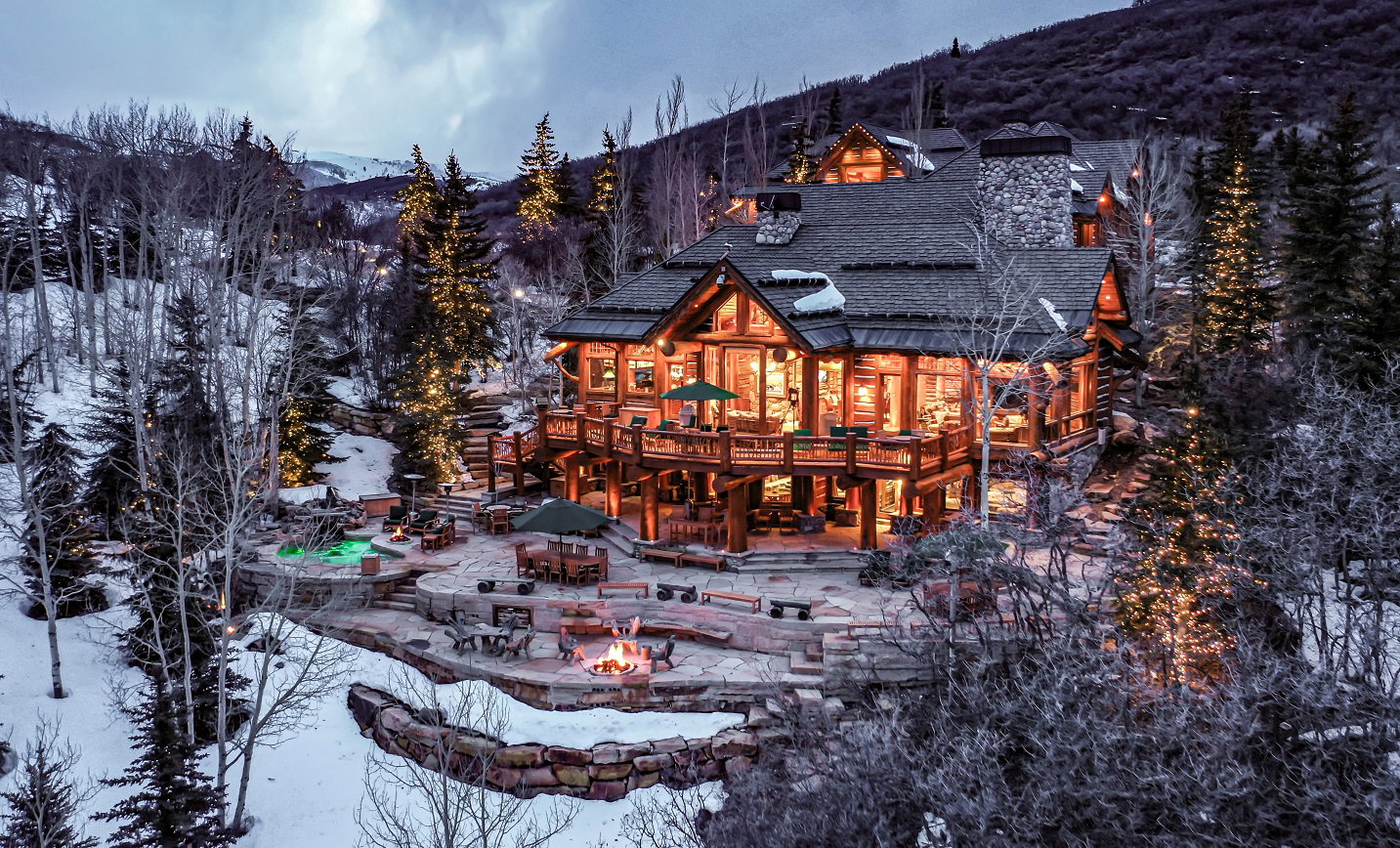 Snow covered back of property featuring a fire pit, a deck with mountain view, and a chimney
