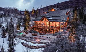 Snow covered back of property featuring a fire pit, a deck with mountain view, and a chimney