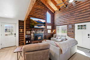 Living room with log walls, a ceiling fan, a high wooden beamed ceiling, a wood stove, and wood finished floors