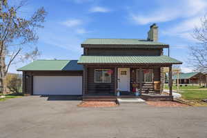 Log cabin featuring log exterior, a porch, a garage, a chimney, and asphalt driveway