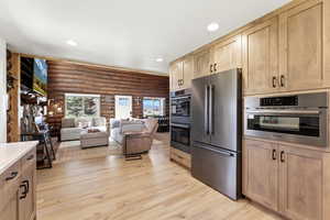 Kitchen featuring log walls, stainless steel appliances, open floor plan, light wood-style flooring, and recessed lighting
