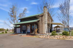 Log-style house with a porch, a metal roof, log exterior, driveway, and a chimney
