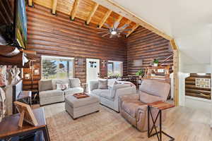 Living room featuring log walls, wood finished floors, healthy amount of natural light, ceiling fan, and a high wooden beamed ceiling