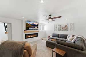 Carpeted living room featuring a ceiling fan, a large fireplace, recessed lighting, and a textured ceiling