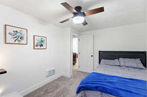 Bedroom with light carpet, ceiling fan, and a textured ceiling