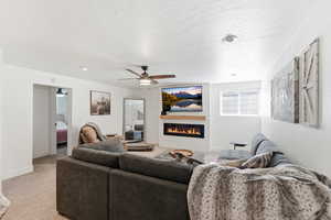 Living area featuring a glass covered fireplace, carpet flooring, a ceiling fan, and a textured ceiling
