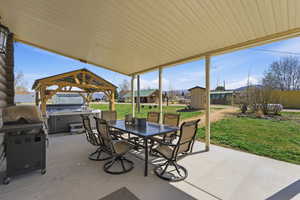 View of patio featuring a hot tub, a gazebo, outdoor dining space, a grill, and a storage unit