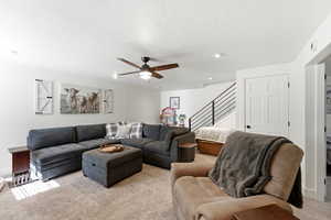 Living area featuring light colored carpet, a ceiling fan, and a textured ceiling