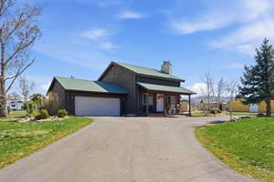 Rustic home featuring a front yard, covered porch, a metal roof, a chimney, and a garage