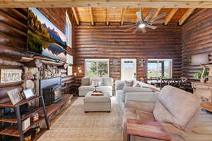 Living area with a wood stove, log walls, a ceiling fan, plenty of natural light, and a vaulted wooden ceiling