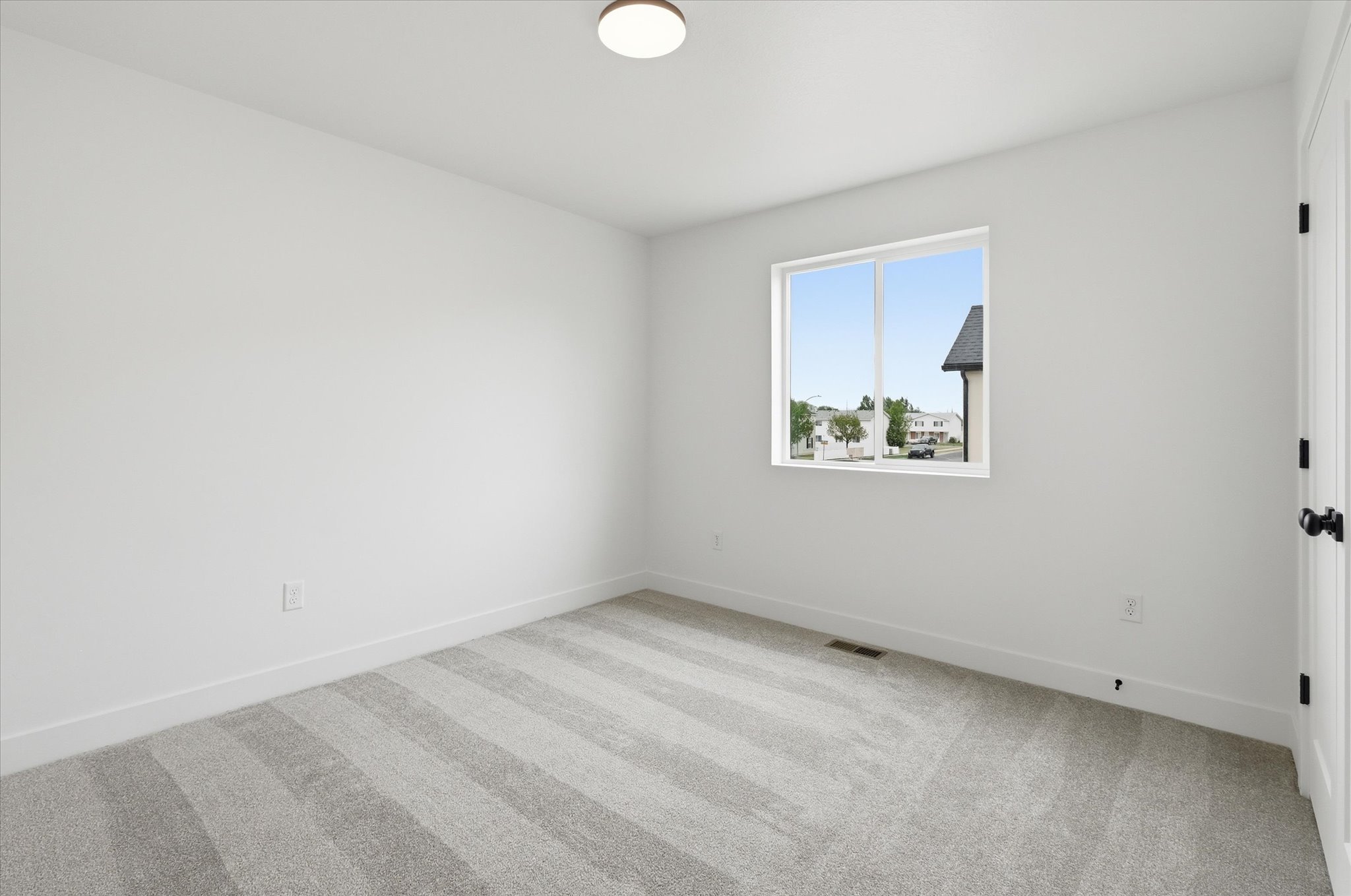 Neutral-toned room featuring a large window, light gray striped carpet, white baseboards, and a contemporary flush-mount ceiling light