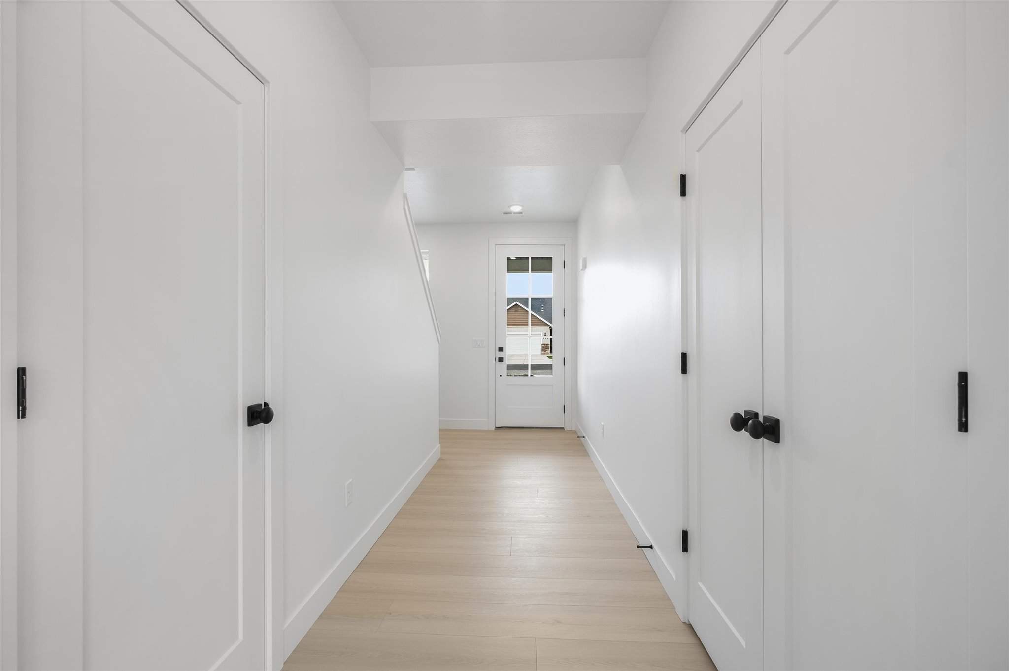 Entry hallway with light wood-finish flooring, white walls, and multiple panel doors featuring matte black hardware