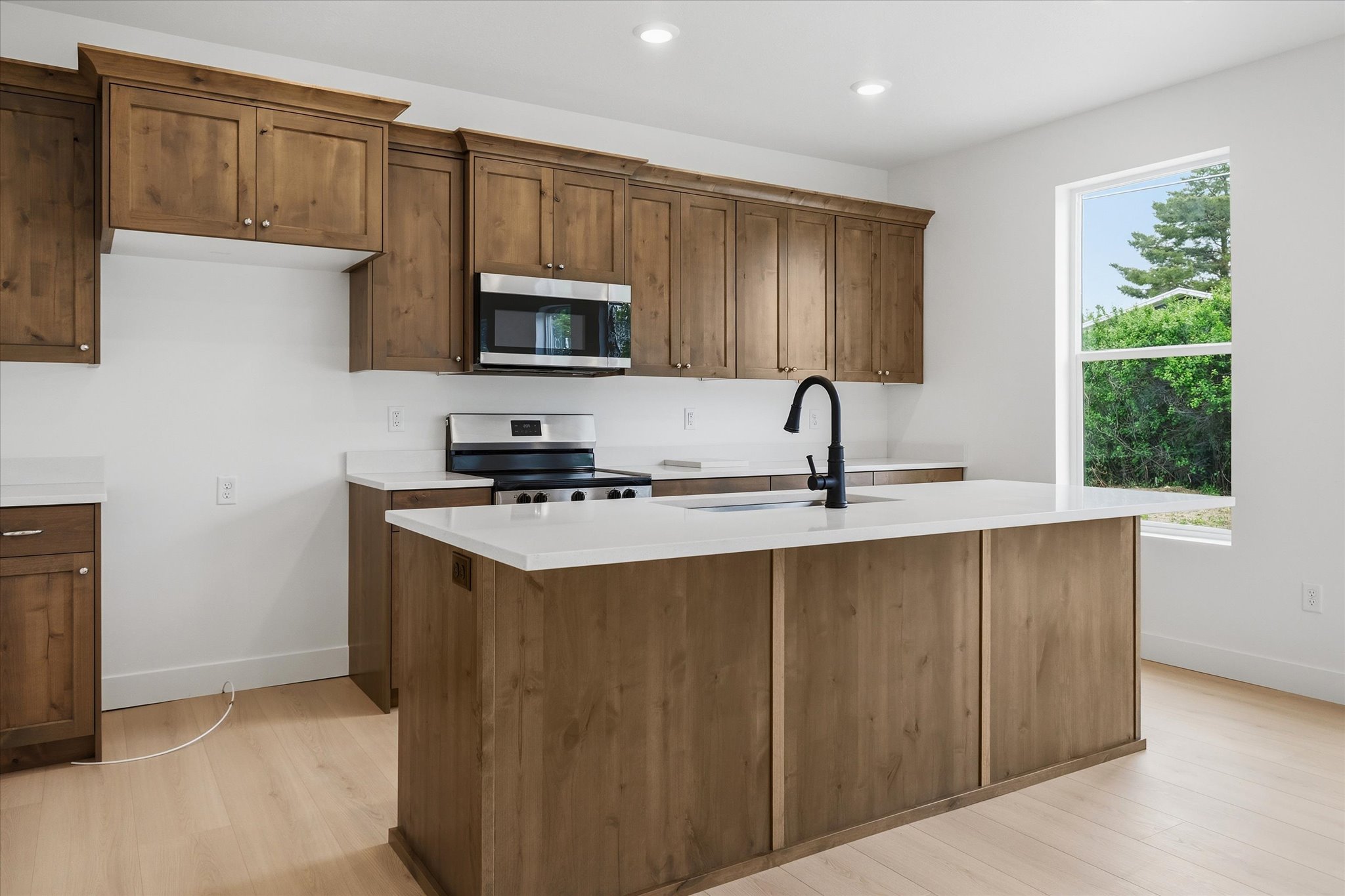 Modern kitchen featuring a central island with an integrated sink, wood-finish cabinetry, stainless steel appliances, white countertops, and light wood-finish flooring