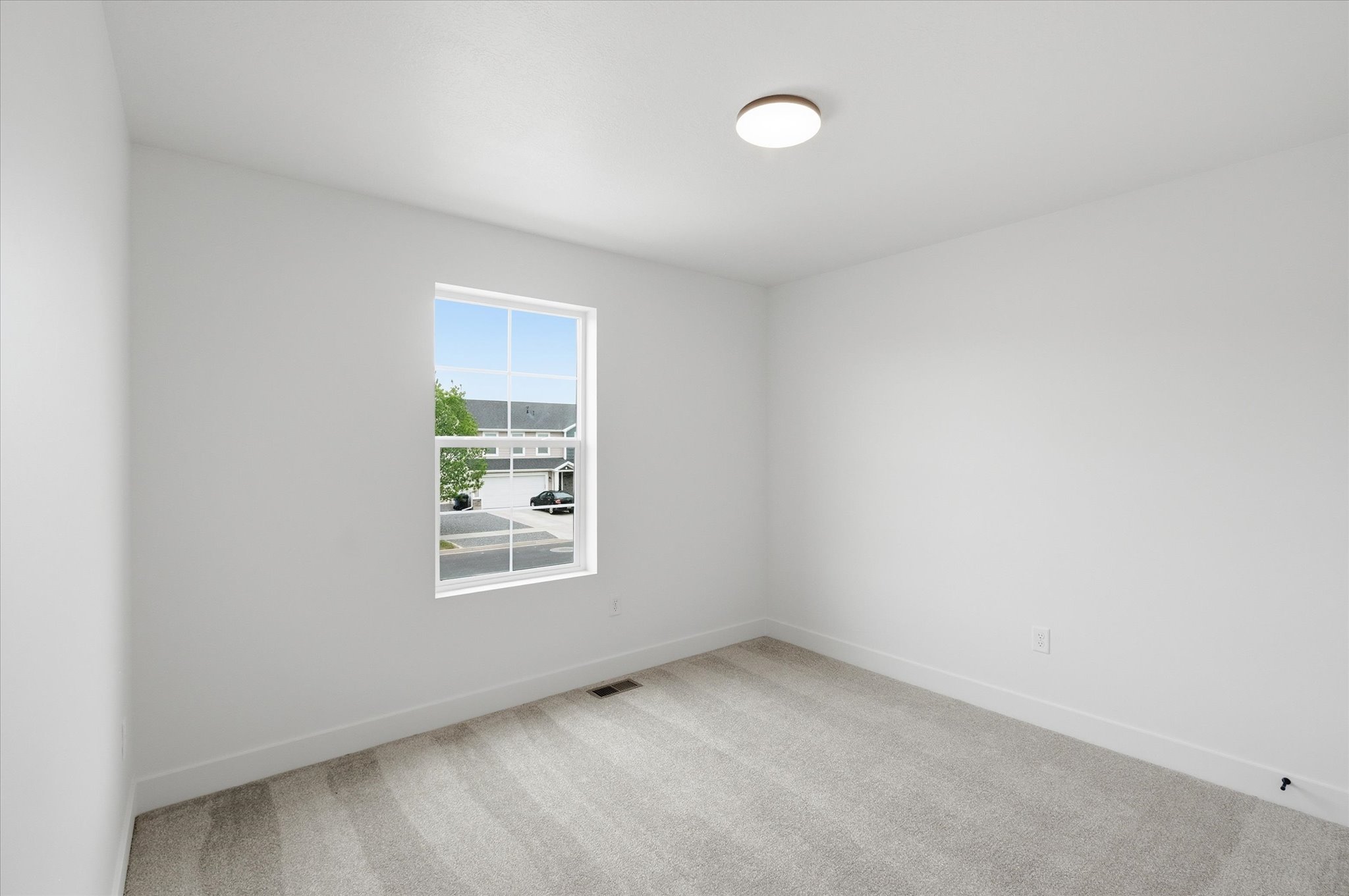 Bright room featuring a large single window, light-colored carpeting, white baseboards, and a flush-mount ceiling light