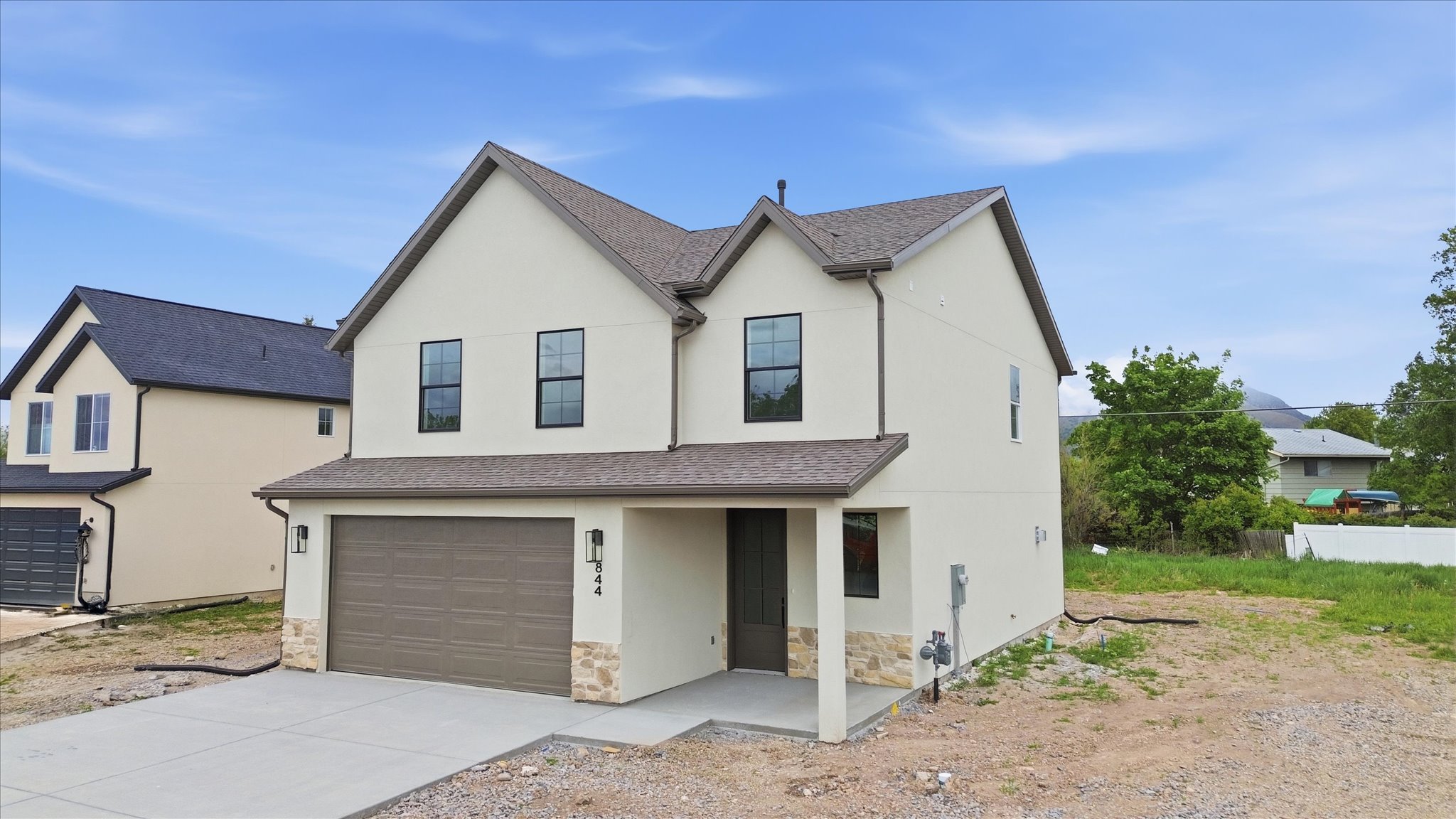 Contemporary two-story residence featuring a light-colored stucco exterior, stone accents, and a dark brown garage door