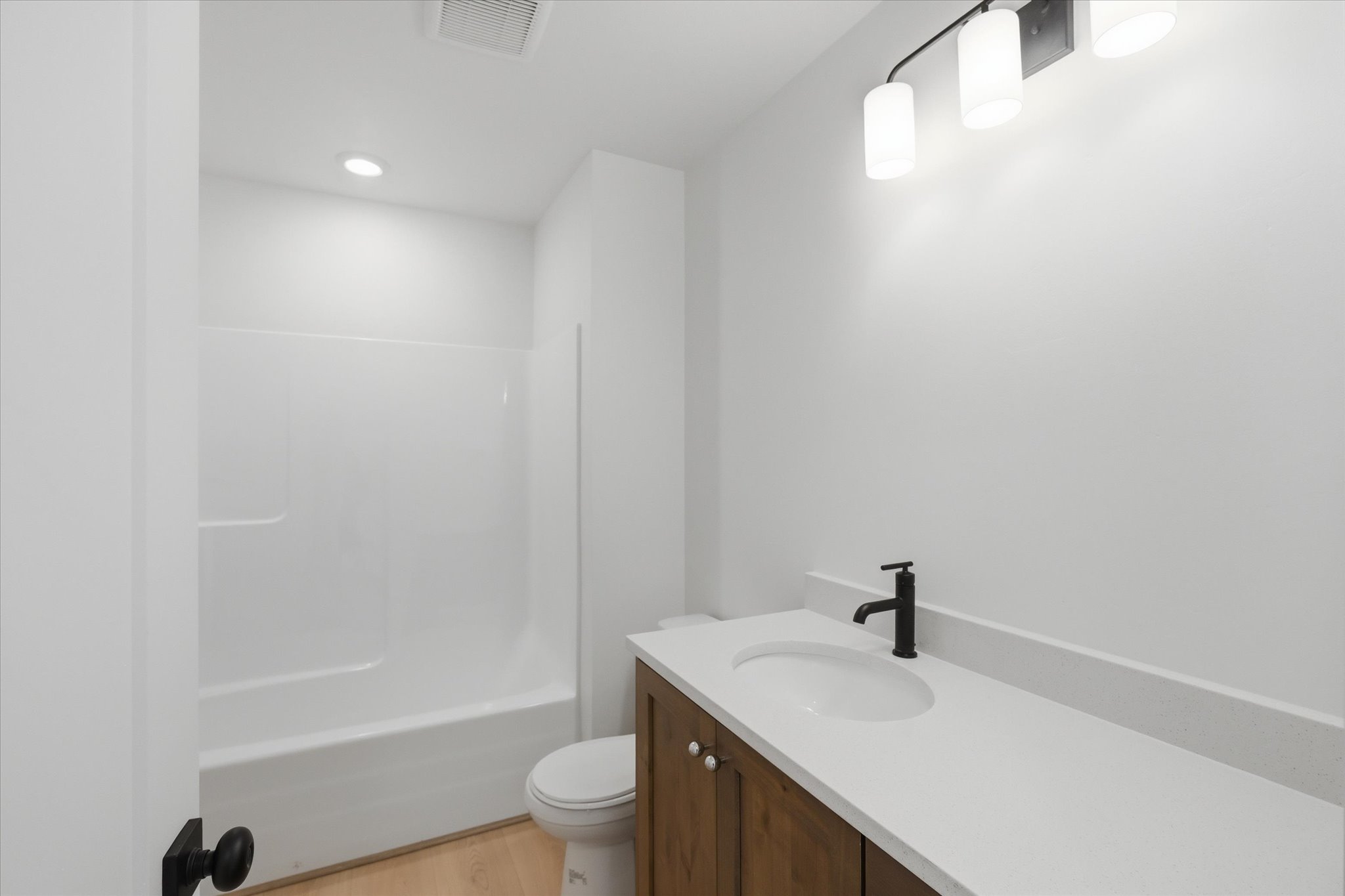 Bathroom featuring a wood-finish vanity with an undermount sink, a light-colored countertop, and a matte black faucet