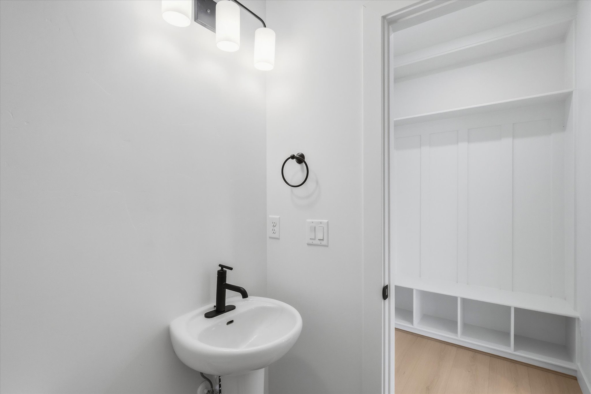 Pedestal sink with a matte black faucet and ring towel holder