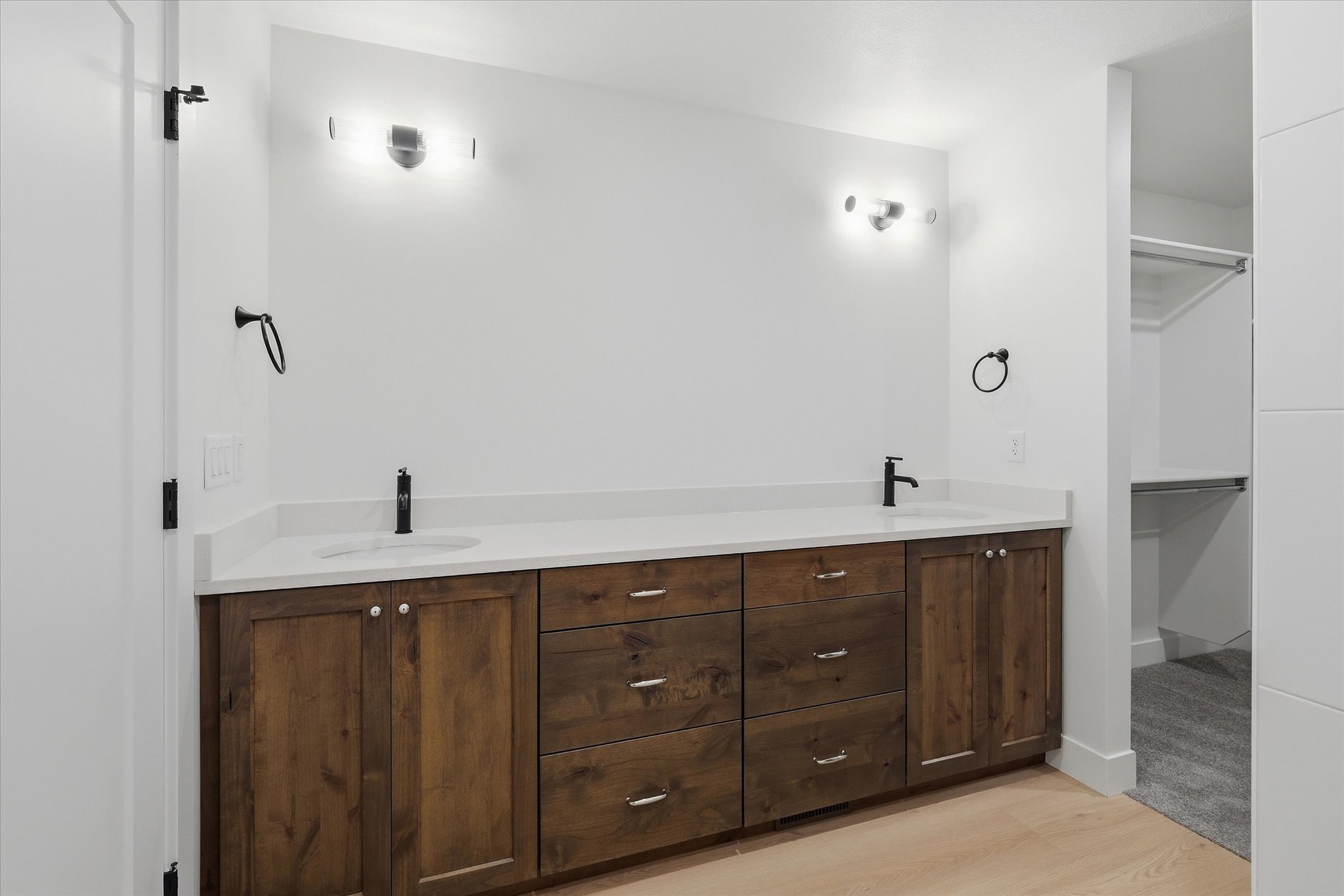 Dual basin vanity with a white countertop, dark wood-finish cabinetry, and matte black fixtures