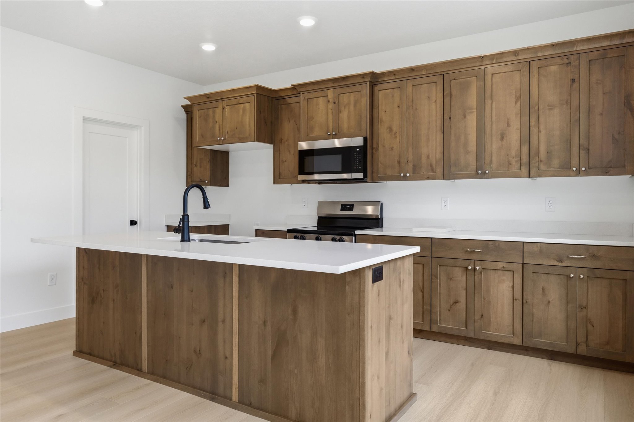 Kitchen featuring an expansive island with a matte black faucet, wood-finish cabinetry, stainless steel appliances, and light-toned flooring