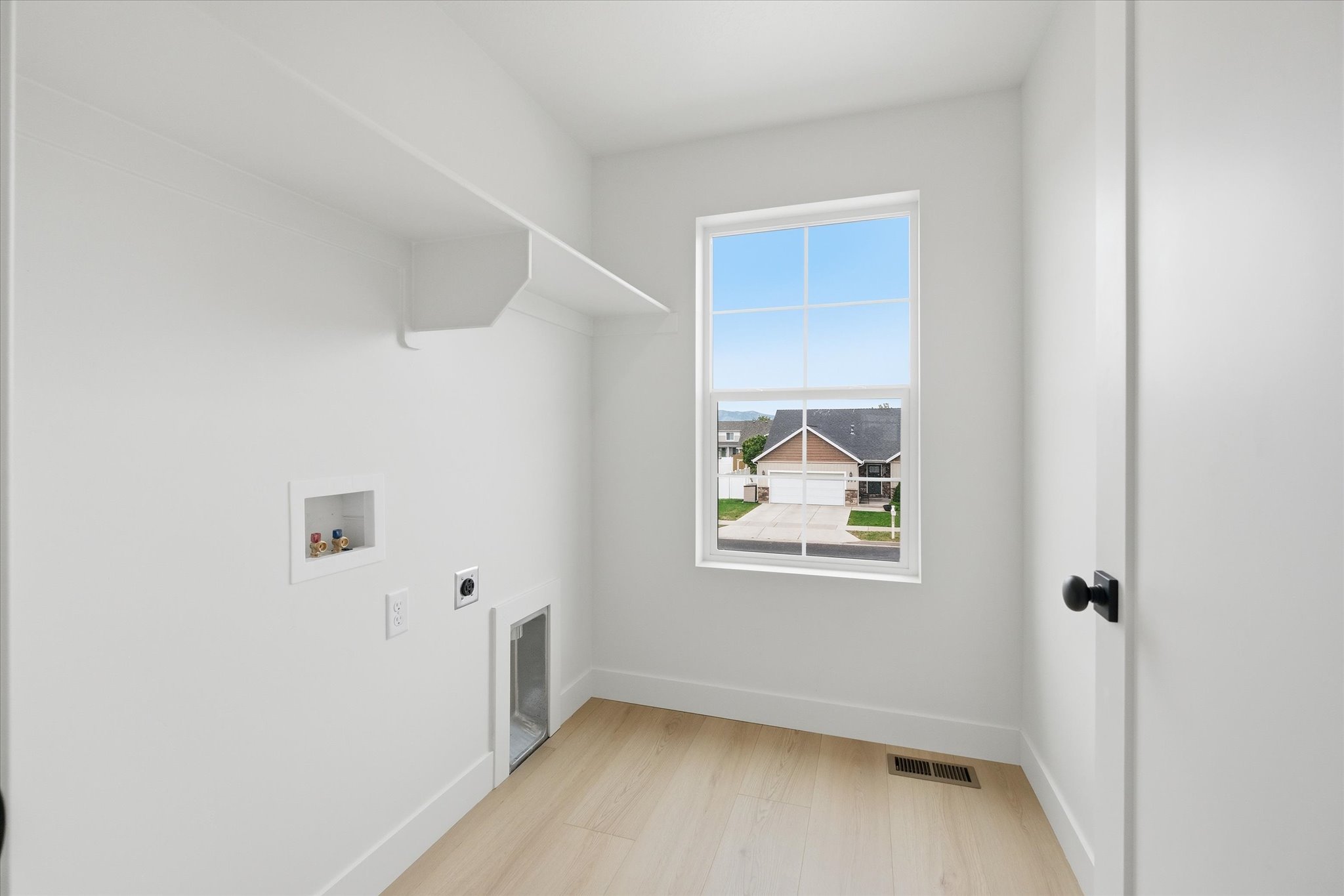 Bright laundry space featuring wood-finish flooring, a white-framed window, and built-in shelving