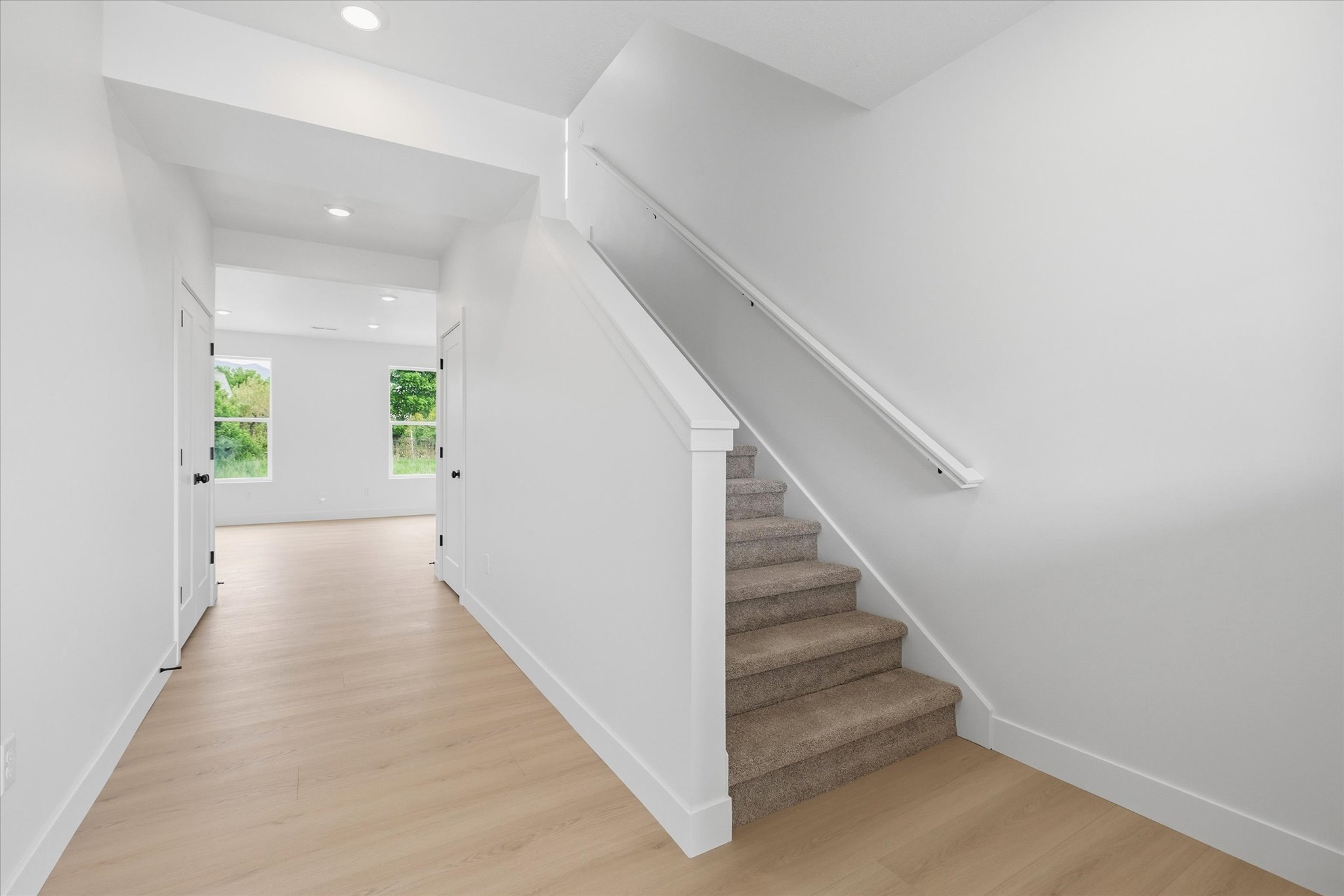 Bright entryway featuring wood-finish flooring, recessed lighting, and a staircase with carpeted treads and a white handrail