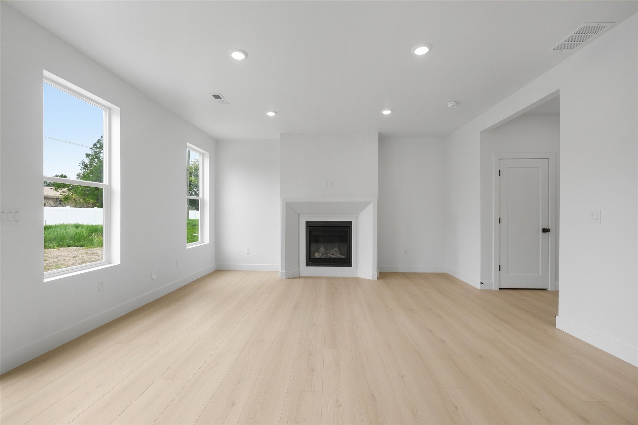 Bright interior featuring wood-finish flooring, a contemporary fireplace with a white mantel, recessed lighting, and large windows