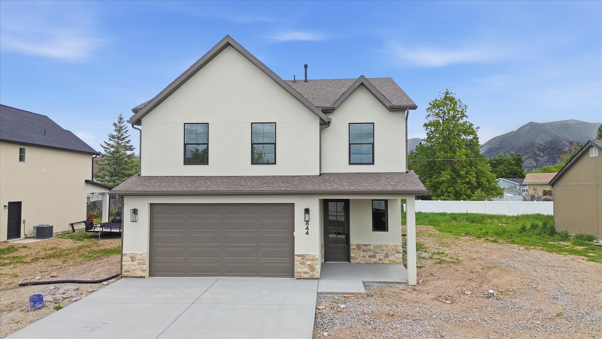 Two-story residence featuring a neutral stucco exterior with stone veneer accents, a covered front porch, and a two-car garage