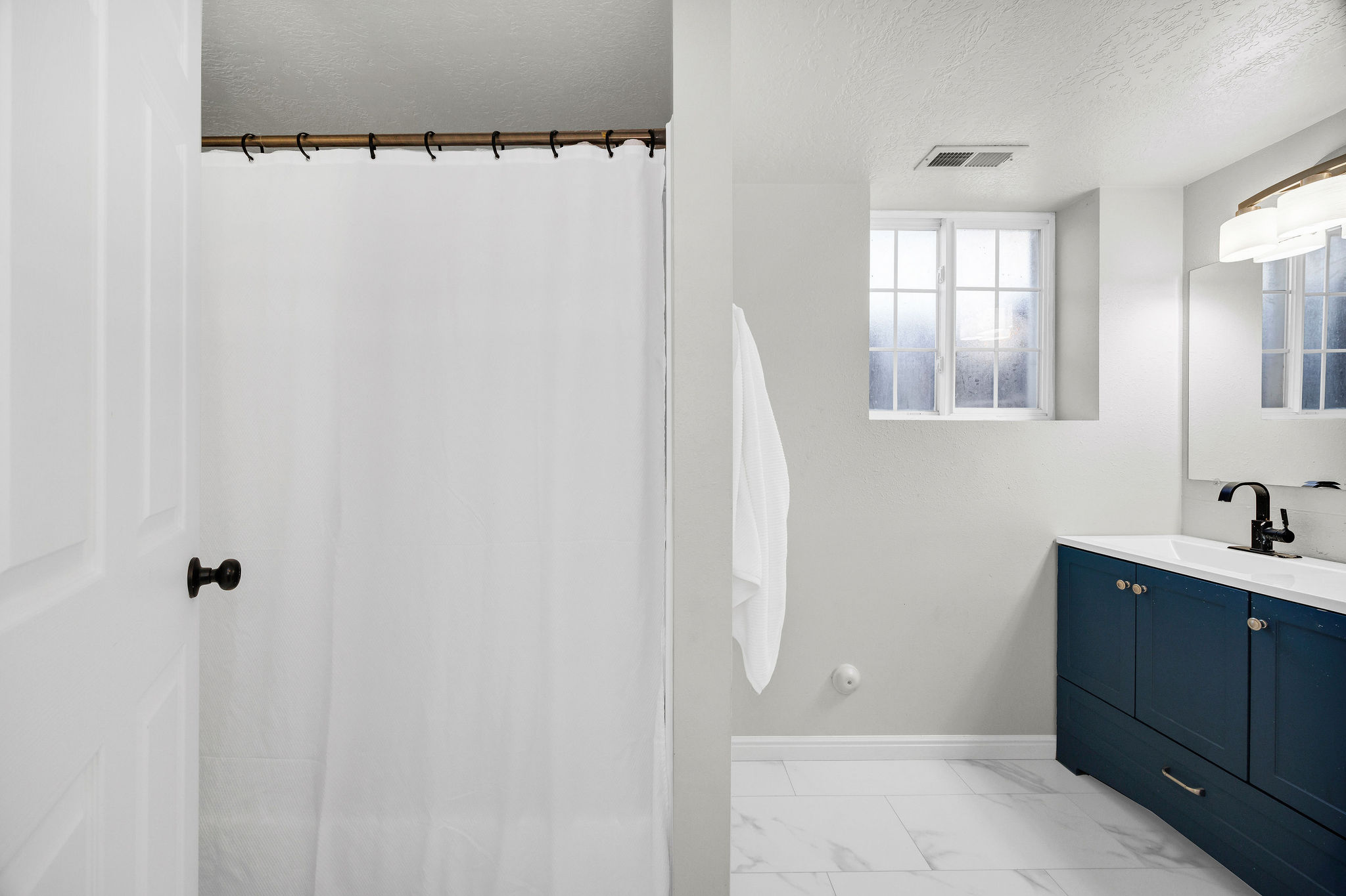 Full bathroom in basement with vanity, a textured ceiling, a shower with shower curtain, and light marble finish floors