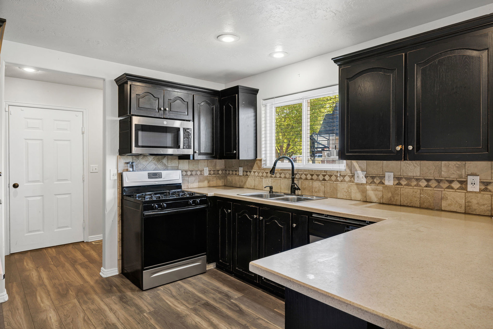 Kitchen featuring black gas range oven, light countertops, dark cabinets, dark wood-style flooring, and stainless steel microwave